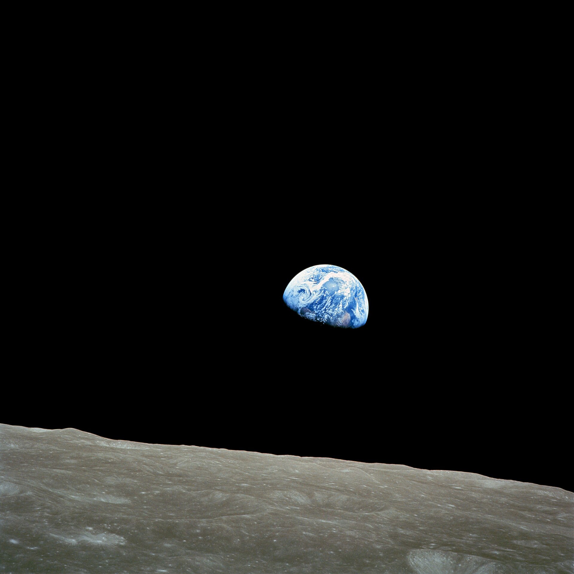 The Earth, half in shadow, rising above the grey cratered surface of the Moon