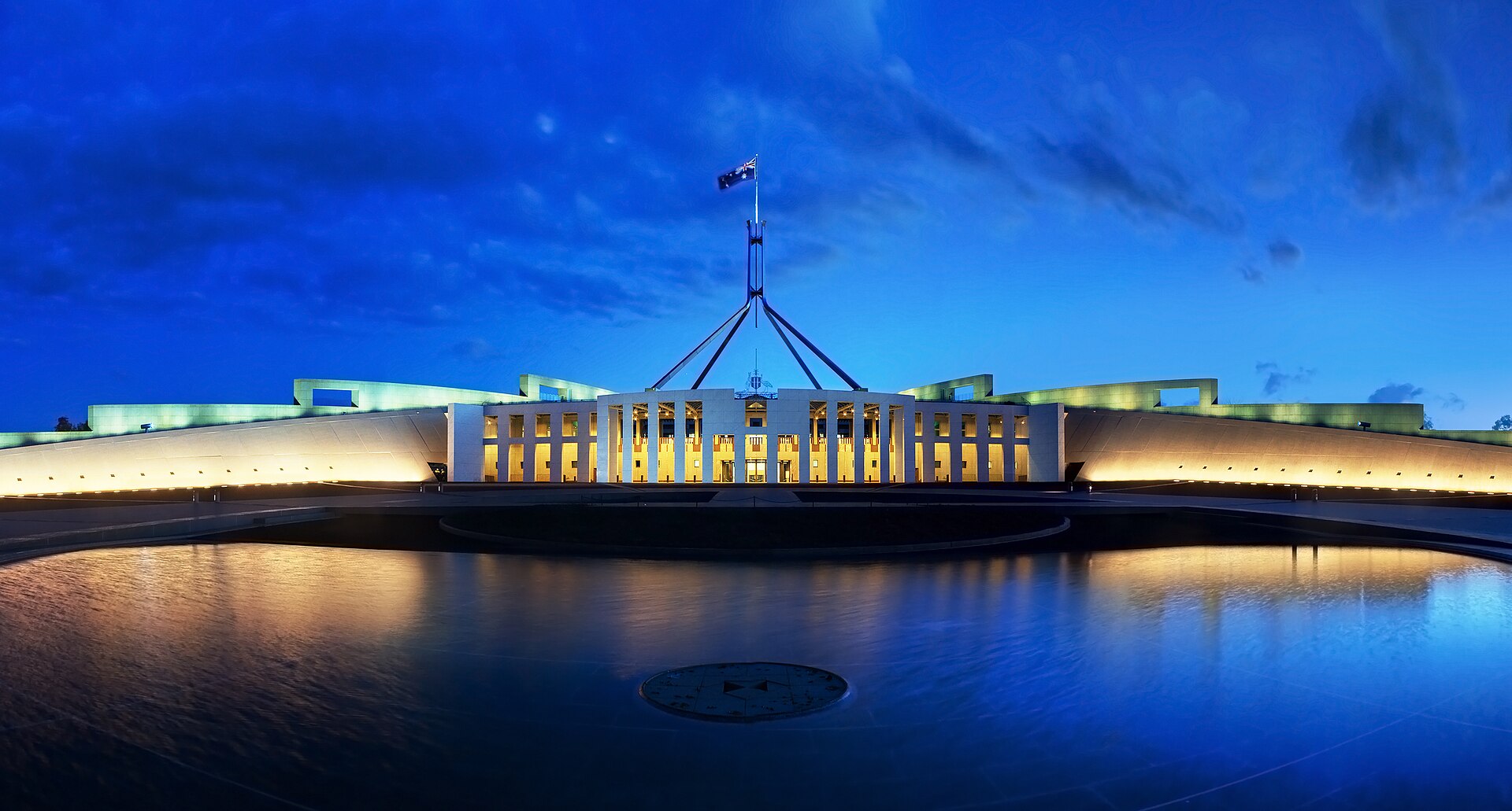 Parliament House, Canberra, seen from the front at dusk, with the flag mast rising from a grassed roof