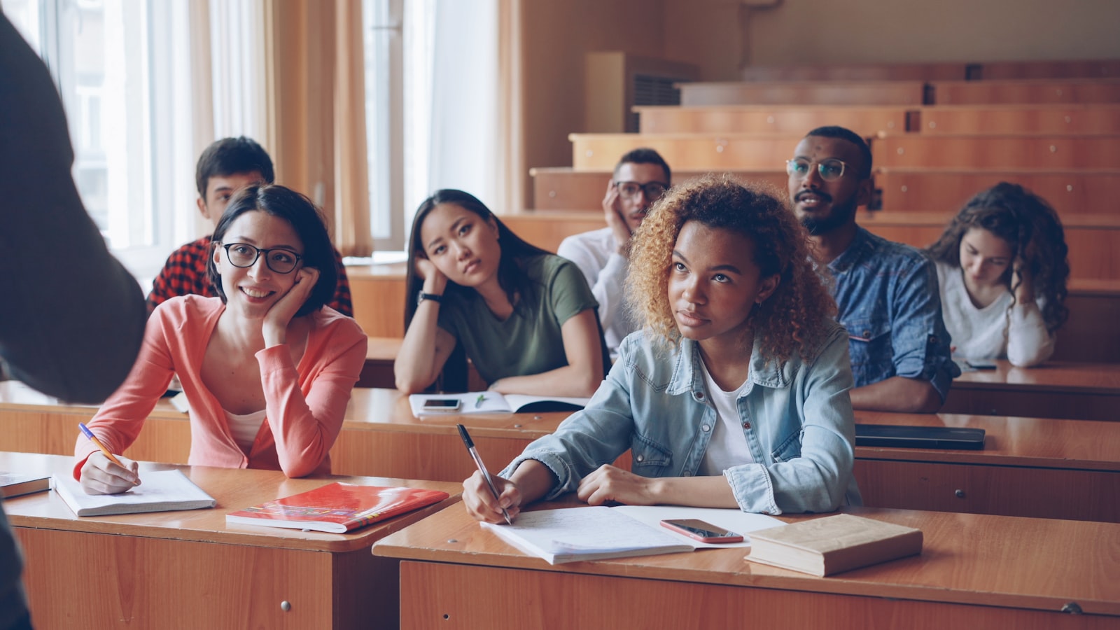 Senior students taking notes at their desks in a classroom while their teacher speaks