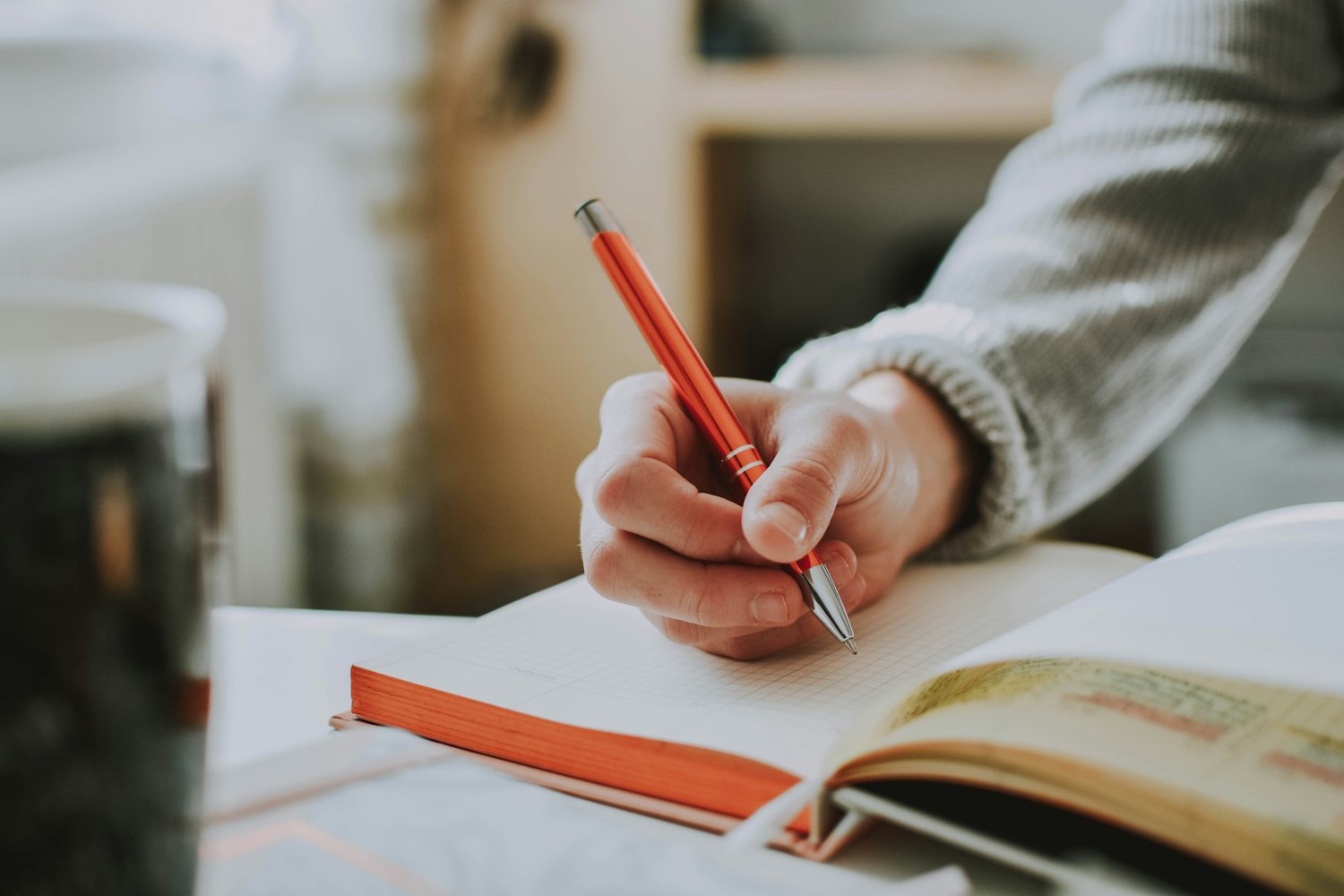 A student writing an essay by hand next to an open book